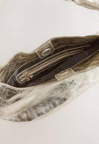 Metalna srebrna torba z teksturiranim zaključkom, ki ima zadrgo in sponke, obložena s temnim materialom.