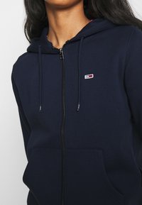 Felpa con zip color navy realizzata in morbido tessuto, caratterizzata da un piccolo logo ricamato, due tasche frontali e cordini regolabili sul cappuccio.