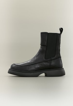 Black leather ankle boot with elastic side panels, thick sole, rounded toe, and pull tab at the back, shown in profile on a neutral background.