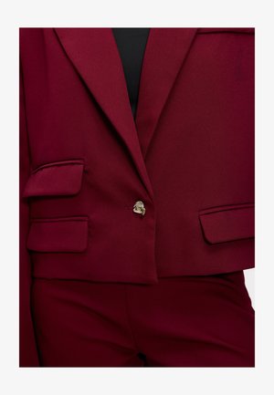 Blazer bordeaux à coupe courte, avec deux poches avant et une fermeture à un bouton. Tissu lisse avec une coupe structurée.