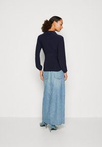 Marineblå langermet topp med krage og rynket detalj bak, kombinert med en lyseblå, høy midje jeansskjørt med frynset kant.