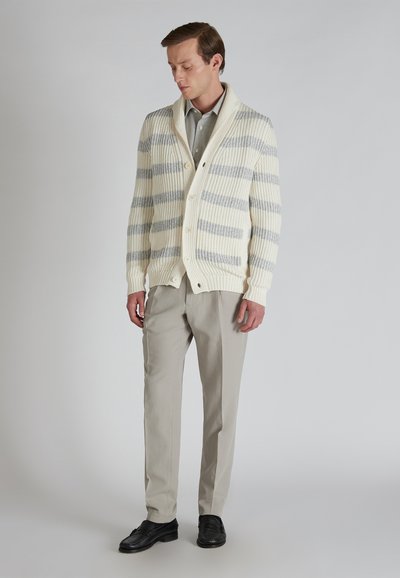 Cárdigan crema con rayas grises, textura acanalada, cuello de chal y cierre de botones. Combinado con pantalones gris claro y zapatos negros.