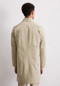 Lichtbeige lange jas met een eenvoudig ontwerp, gemaakt van gladde stof, met een rechte snit en een klassieke kraag, gezien vanuit de achterkant.