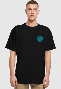 Camiseta negra de algodón, con un gráfico circular turquesa que dice "BAILE BAJO LAS ESTRELLAS" en la zona del pecho izquierdo.