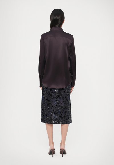 Tume lilla satiinist särk pikkade varrukatega, paaritatud põlveni ulatuva mereväe sinise litritega seelikuga, millel on lillemustrid ja sirge äärejoon.