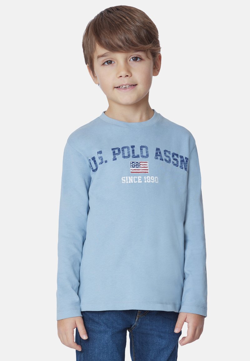 Maglietta a maniche lunghe di colore azzurro chiaro con testo "U.S. POLO ASSN" e grafica della bandiera americana. Realizzata in morbido tessuto di cotone.