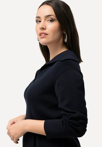Suéter de punto azul marino con un cuello amplio, mangas largas y una silueta ajustada. Textura suave y sin patrones ni adornos visibles.