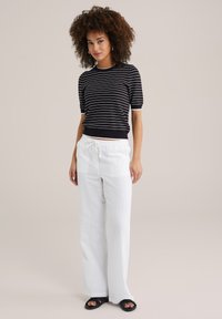 Zwart-wit gestreepte top met korte mouwen, gecombineerd met losse witte broek met trekkoord en open zwarte sandaaltjes op een lichte achtergrond.