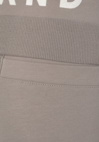 Hellgrauer Sweatshirtstoff mit einem gerippten Taillenbund. Mit weißem Text und einer Seitentasche. Weiche Textur und minimalistisches Design.