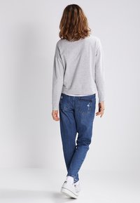 Sudadera gris de corte relajado, combinada con unos vaqueros de mezclilla azul con un ligero desgaste y pierna ajustada. Zapatillas blancas completan el look.