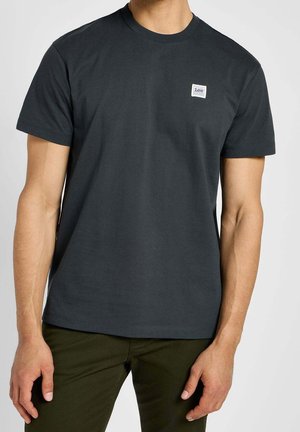 T-shirt à manches courtes gris foncé en coton avec col rond, comportant une petite étiquette blanche sur la poitrine. Couleur unie, sans motifs.