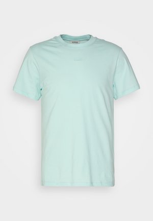 Jasnoniebieska bawełniana koszulka z okrągłym dekoltem, zestawiona z ciemnoszarymi spodniami w kant i czarnymi botkami za kostkę. Prosty design, bez widocznych wzorów.