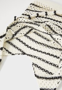 Knit scarf in cream with black horizontal stripes and openwork details. Features varying textures and patterns throughout the fabric.