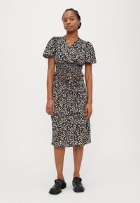 Svart blomsterkjole med korte pufferm, smokkebodice og midilengde. Har en snor i livet og små flerfargede blomster mønstre.