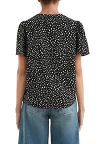 Schwarzes Oberteil mit weißem unregelmäßigem Punktmuster, kurzen Puffärmeln, runder Ausschnitt und leicht gerafftem Saum, kombiniert mit blauen weit geschnittenen Jeans.