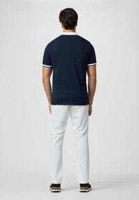 Námornícky polo tričko s bielym golierom a akcentmi na manžetách, v kombinácii s bielymi nohavicami a tmavými teniskami. Viditeľné švy a detaily strihu.