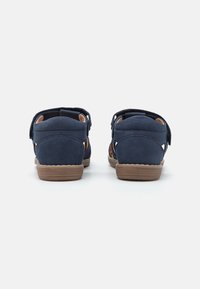 Zapatos de ante azul marino con detalles de corte, correas ajustables y una suela de goma marrón, con un tacón bajo y una textura suave.