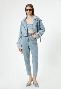 Denim takki ja lyhyt toppi vaaleansinisinä, yhdistettynä korkeavyötäröisiin vaaleansinsisiin farkkuihin ja korkokenkiin. Materiaali näyttää pehmeältä ja siinä on hieman tekstuuria.