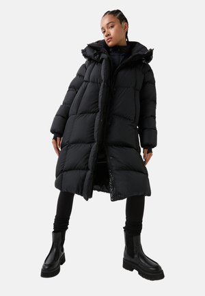 Black puffer coat featuring a hood and a zip-front, with a quilted design and ribbed cuffs, paired with black ankle boots.