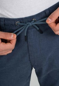 Blue drawstring pants made of textured fabric, featuring a metal eyelet and contrasting drawstring with plastic tips.