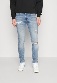 Ljusblå, slitna skinny jeans med slitna detaljer och subtila blekningar. Matchas med vita högskurna sneakers med blå accenter.