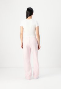 White fitted t-shirt and light pink sweatpants, featuring an elastic waistband and wide legs, made from soft fabric. Plain design.
