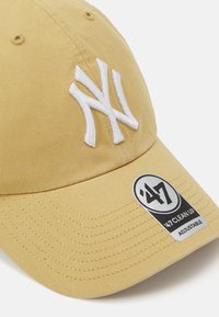 Gelbe Baumwoll-Baseballmütze mit verstellbarem Riemen, ausgestattet mit einem weißen gestickten "NY"-Logo und einem schwarzen runden Etikett mit der Aufschrift '47 Clean Up'.