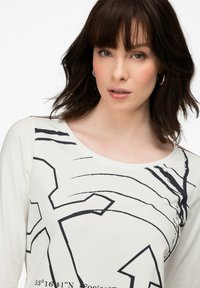 Weißes Langarmshirt mit schwarzen abstrakten Grafiken, einschließlich Linien und Formen, einem weiten Ausschnitt und weichem Material.