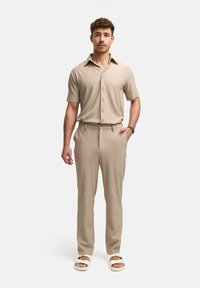 Lichtbeige geribbelde korte mouwen overhemd met knopen, gecombineerd met bijpassende taps toelopende broek. Gemaakt met witte open teen sandalen. Eenvoudig ontwerp en casual pasvorm.