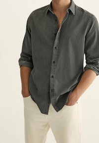 Grijs overhemd met knopen en lange mouwen, zacht van textuur, losse pasvorm en enkele knopen open, gecombineerd met lichtgekleurde broek.