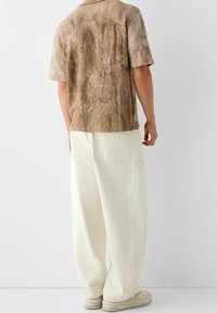 Korte mouwen, bruin gestructureerd shirt met een mesh-patroon, gecombineerd met losse, crèmekleurige broek en beige sneakers.