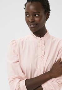 Cămașă roz deschis cu guler și manșete volane. Material moale, textură discretă și croială clasică. Prezentă butoane mici pe toată lungimea frontală.