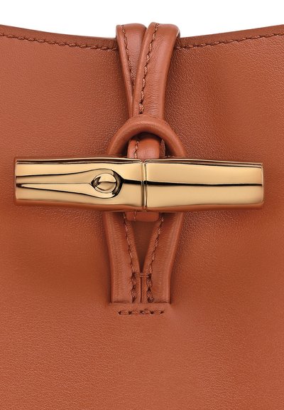 Nahaufnahme einer braunen Lederhandtasche mit einem goldfarbenen Verschluss, glatter Oberfläche und genähten Akzenten, die ein elegantes Design und eine strukturierte Form präsentiert.