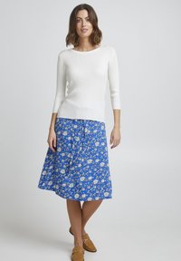 Weißer gerippter Strickpullover mit Dreiviertelärmeln, kombiniert mit einem blauen Rock mit Blumenmuster, knielang, und braunen Slippern.