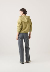 Khaki színű, kapucnis pulóver, laza szabással, amelyet magas derekú szürke farmerral viselnek. Az öltözet finom varrási részletekkel és minimalista dizájnnal rendelkezik.