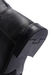 Stivale alla caviglia in pelle nera con punta rotonda, superficie texturizzata e un distintivo tacco in gomma piatto con un sottile dettaglio di design.