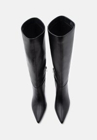 Par crnih kožnih čizama do koljena s izduženim vrhovima i bočnim patentnim zatvaračima, fotografirani iz ptičje perspektive na bijeloj pozadini.