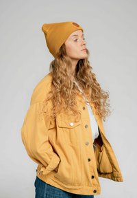 Żółta dżinsowa kurtka z zamkami na srebrne guziki, z dużymi kieszeniami i luźnym krojem, w zestawie z dopasowaną żółtą czapką z ribbingu.