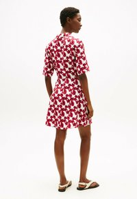 Vestito a maniche corte con base bianca e motivo floreale rosso. Il design presenta una silhouette aderente e una gonna svasata, con scollo a collo.