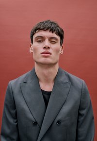 Hall jahekate neljasilmusega särk, millel on tekstuuriline kangas ja mustad nupud. Teema juuksed on lühikesed ja tumedad ning tal on seljas must särk.