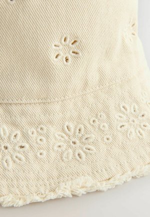 Kreminės spalvos audinio kibirėlio skrybėlė su gėlių siuvinėjimu ir nutrinta briauna. Tekstūra yra minkšta, su vertikaliais briauneliais.