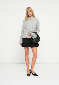 Γκρίζα πλεκτή ζακέτα με στρογγυλή λαιμόκοψη, κουμπιά μπροστά και ζωνάκι στη μέση. Σε συνδυασμό με μια μαύρη φουστάνι με βολάν και μια μαύρη τσάντα. Μαύρα παπούτσια με τακούνι.