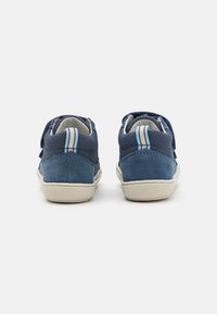 Navy blue sneakers with suede and mesh materials, white rubber soles, and blue-striped heel tabs. Ankle-high cut with lace closure.
