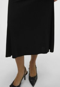 Črna midi krila z gladko teksturo in razširjenim robom, v kombinaciji z ozkimi črnimi slingback petami z okrasnimi pentljami.