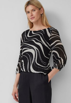 Blusa a righe bianco e nero con un tessuto liscio, ampio scollo a barca e maniche a sbuffo. Abbinata a pantaloni scuri e larghi.