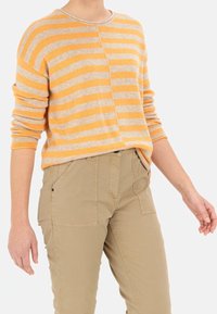 Gestreifter Pullover in Orange und Beige, aus weichem Stoff. Lange Ärmel, Rundhalsausschnitt und lockerer Schnitt. Kombiniert mit hellbeigen Hosen.