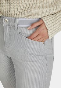 Grijs en witte gestreepte jeans met een middelhoge taille, voorzien van voorkruiszakken en een metalen knoopsluiting. Zacht, textuurstof met stiksels.