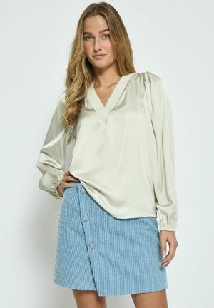 Light beige satin blouse with a V-neck and puff sleeves, paired with a blue textured skirt featuring a side button closure.