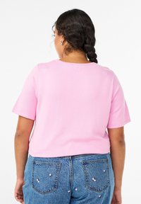 Īsās piedurknes rozā adīta topiņa ar apaļu izgriezumu, kombinēta ar zilām džinsa biksēm, kurām uz aizmugurējām kabatām ir dekoratīvi ķiršu motīvi.