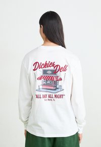 White long-sleeve shirt featuring a graphic of a deli cart with a red and white striped awning, text reading “Dickies Deli" and "All Day All Night."